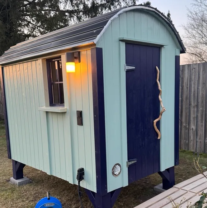Bauwagen-Sauna in Hellblau und Dunkelblau mit Außenleuchte und Astgriff am Abend
